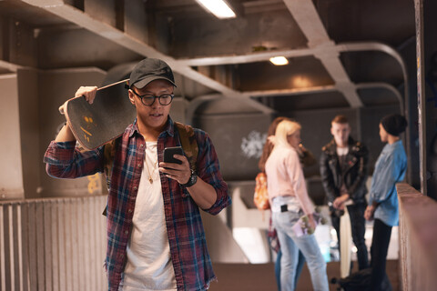 Junger männlicher Skateboarder schaut auf einer Fußgängerbrücke auf sein Smartphone, lizenzfreies Stockfoto