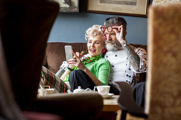 Skurriles Vintage-Paar, das in der Teestube auf sein Smartphone schaut - CUF10799