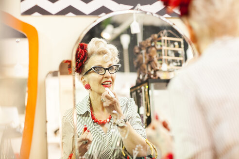 Mirror image of quirky vintage woman applying lipstick in antique and vintage emporium - CUF10803