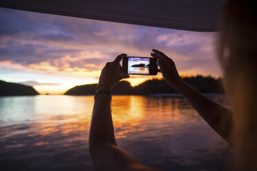 Woman photographing sunset with smartphone, Koh Rok Noi, Thailand, Asia - CUF10850