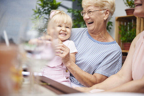 Ältere Frau lacht mit ihrer kleinen Enkelin beim Familienessen auf der Veranda - CUF10862