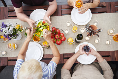 Draufsicht auf eine Familie, die beim Familienessen auf der Terrasse Salate verteilt - CUF10863