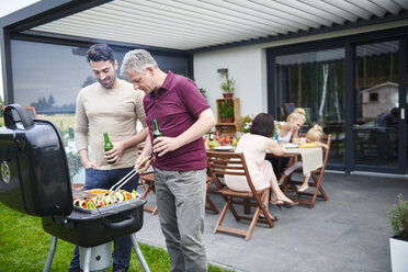 Mature and mid adult man barbecuing at family lunch on patio - CUF10864