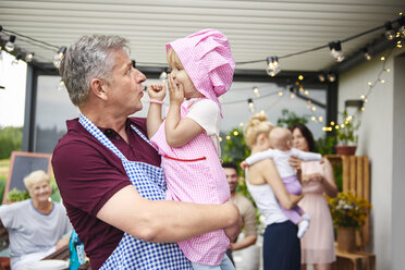 Mature man making faces at toddler granddaughter at family lunch on patio - CUF10870