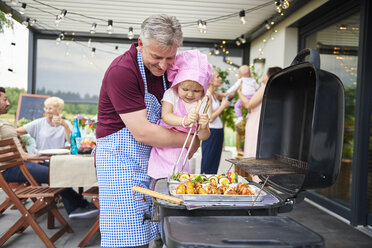 Female toddler barbecuing with grandfather at family lunch on patio - CUF10871