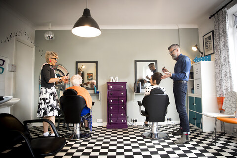 Ehepaar in Vintage-Kleidung bei der Arbeit an Kunden in einem skurrilen Friseursalon, lizenzfreies Stockfoto