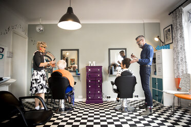 Couple in vintage clothes working on customers in quirky hair salon - CUF10877