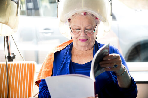 Female customer reading magazine in hair salon - CUF10881