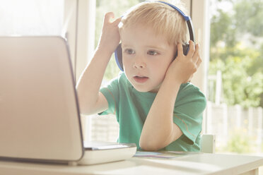 Boy at desk using laptop and listening to headphones - CUF10889