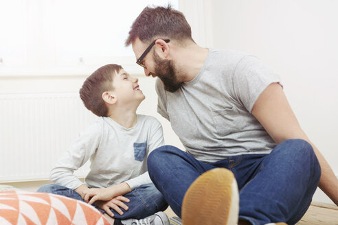 Vater und Sohn sitzen auf dem Boden und lächeln sich gegenseitig an - CUF10893