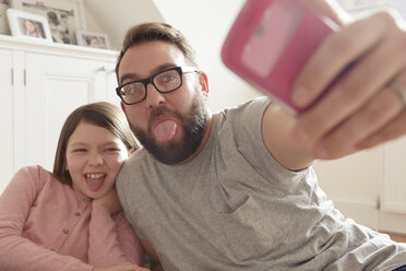 A father and his daughter capture a moment together with a selfie on their smartphone - CUF10898