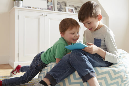 Männliches Kleinkind und Bruder auf Sitzsackstuhl mit Blick auf ein digitales Tablet - CUF10902