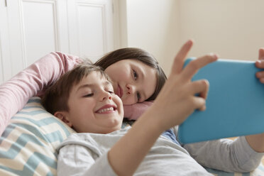 Boy and sister reclining on beanbag chair looking at digital tablet - CUF10904