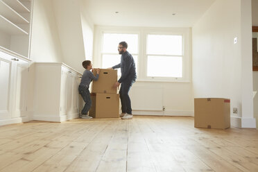 Mid adult man and son stacking cardboard box in new home - CUF10911
