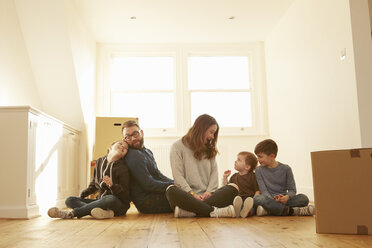 Mittleres erwachsenes Paar und drei Kinder sitzen auf dem Boden in der neuen Wohnung - CUF10912