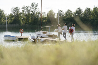 Freunde gehen auf ein Segelboot zu, tragen Ausrüstung, langes Gras im Vordergrund - CUF10956