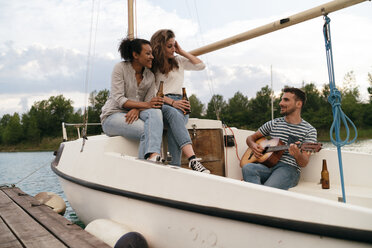 Drei Freunde entspannen sich auf einem vertäuten Segelboot, trinken Bier, der Mann spielt Gitarre - CUF10964