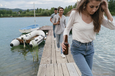 Three friends walking along pier, holding bottled beer - CUF10967