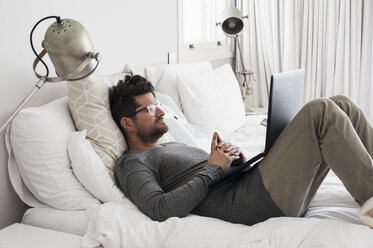 Mittlerer erwachsener Mann auf dem Bett liegend, Laptop benutzend - CUF11092