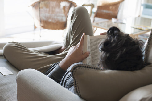 Mittlerer erwachsener Mann, der sich auf dem Sofa entspannt und ein Buch liest, Rückansicht - CUF11094