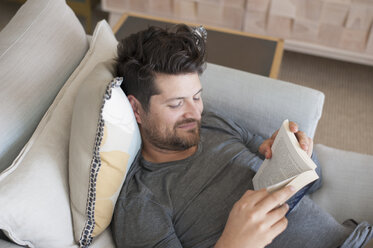 Mittlerer erwachsener Mann entspannt sich auf dem Sofa, liest ein Buch, Blick von oben - CUF11095