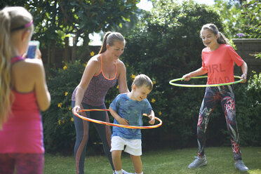 Mädchen fotografiert Mutter und Geschwister beim Hoola Hooping im Garten - CUF11107