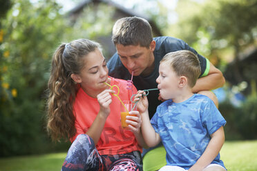 Älterer Mann mit Tochter und Sohn im Teenageralter teilt sich einen frischen Smoothie im Garten - CUF11190