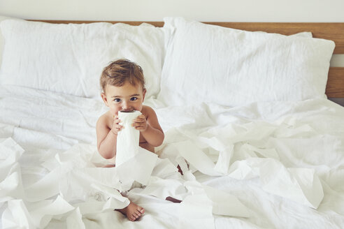 Kleinkind auf dem Bett sitzend, mit aufgerollter Toilettenpapierrolle - CUF11205