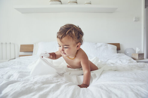 Kleinkind auf dem Bett sitzend, mit aufgerollter Toilettenpapierrolle - CUF11210