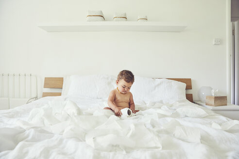 Kleinkind auf dem Bett sitzend, mit aufgerollter Toilettenpapierrolle - CUF11211