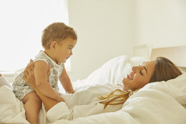 Mother relaxing on bed with toddler, smiling - CUF11214