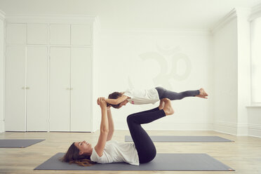 Mother and daughter in yoga studio, daughter balancing on mothers legs - CUF11219