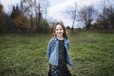 Young girl smiling in field in denim jacket, Lakefield, Ontario, Canada - CUF11273