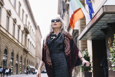 Ältere Frau mit langen grauen Haaren und Koffer auf Rädern vor einem Hotel in Florenz, Italien - CUF11276