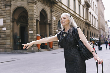 Ältere Frau mit langen grauen Haaren und Koffer auf Rädern hält ein Taxi in Florenz, Italien, an - CUF11277