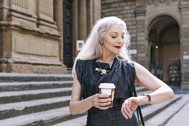Ältere Frau mit langen grauen Haaren schaut auf ihre Armbanduhr in Florenz, Italien - CUF11278