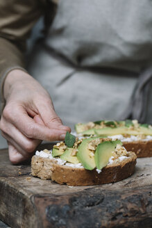 Frau legt Kräuter auf Ricotta, Avocado und Walnuss-Bruschetta, Nahaufnahme - CUF11307