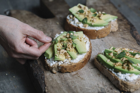 Frau legt Kräuter auf Ricotta, Avocado und Walnuss-Bruschetta, Nahaufnahme - CUF11308