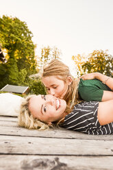 Mother and daughter lying on wooden decking outdoors - CUF11335