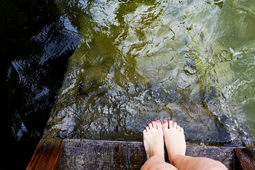 Woman's feet at edge of wooden pier by water - CUF11337