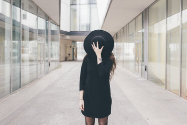 Portrait of young woman in urban environment, covering face with hat - CUF11353