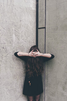 Porträt einer jungen Frau, die in einer Ecke steht, die Haare verdecken das Gesicht, die Hände vor den Haaren verschränkt - CUF11355
