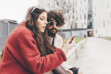 Young couple sitting outdoors, looking at smartphone - CUF11360