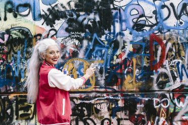 Porträt einer reifen Frau in Baseballjacke, die Graffiti auf eine Wand sprüht - CUF11375