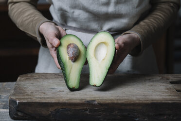 Frau hält halbierte Avocado, Mittelteil - CUF11387