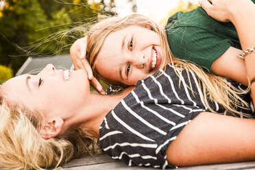 Mother and daughter lying on wooden decking outdoors - CUF11393