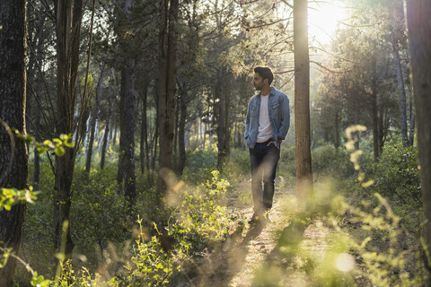Junger Mann im Wald stehend, gegen die Sonne, lizenzfreies Stockfoto