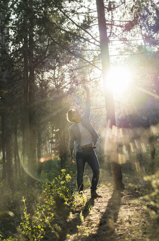 Young man standing in forest, against the sun stock photo