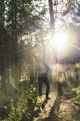 Young man standing in forest, against the sun - AFVF00474