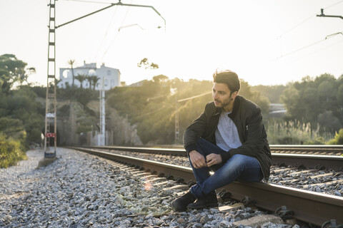 Junger Mann sitzt auf einem Bahngleis, lizenzfreies Stockfoto